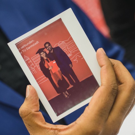 Foto von Absolvent:innen von Hand vor blauem Anzug gehalten 