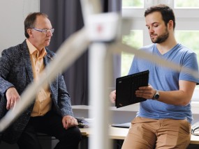 Im Hintergrund unterhalten sich Prof. Max Mühlhäuser und Doktorand Rolf Egert. Im Vordergrund ein unscharfes Windrad.