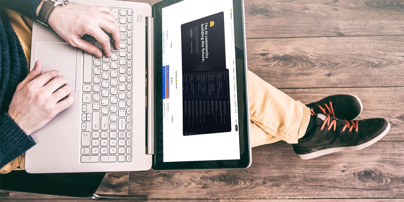 Person sitzt auf einem Holzboden und arbeitet an einem Laptop, auf dessen Bildschirm eine Website zum Thema künstliche Intelligenz geöffnet ist.