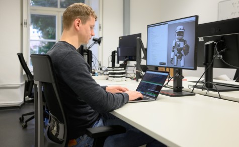 Informatik-Doktorand Felix Friedrich sitzt an einem Schreibtisch vor einem bildschirm und tippt auf einer Tastatur.
