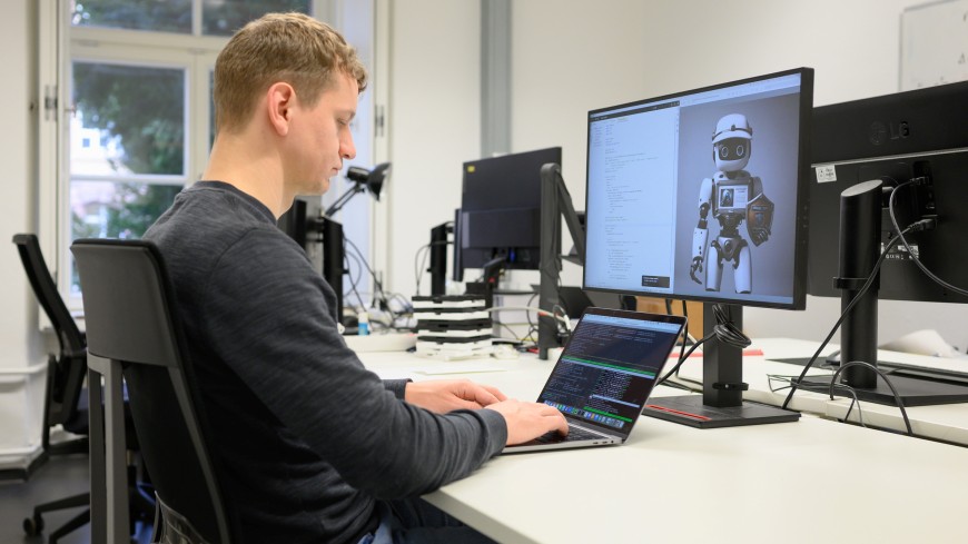 Informatik-Doktorand Felix Friedrich sitzt an einem Schreibtisch vor einem bildschirm und tippt auf einer Tastatur.