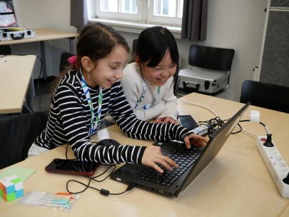 Zwei Schülerinnen sitzen freudig vor einem Laptop und lösen gemeinsam eine Aufgabe