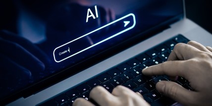 Hände tippen auf einer Laptop-Tastatur, auf dem Bildschirm steht „AI“ über einer Suchleiste mit dem Textanfang „Create a“.