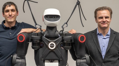 Dr. Oleg Arenz and Professor Jan Peters from the IAS Group at TU Darmstadt standing next to a PAL Robotics humanoid robot, with their hands resting on its shoulders.