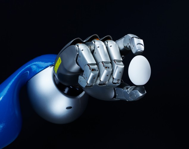 Roboterhand hält ein Ei zwischen Zeigefinger und Daumen vor schwarzem Hintergrund