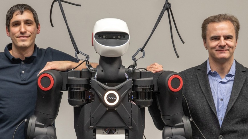 Dr. Oleg Arenz and Professor Jan Peters from the IAS Group at TU Darmstadt standing next to a PAL Robotics humanoid robot, with their hands resting on its shoulders.